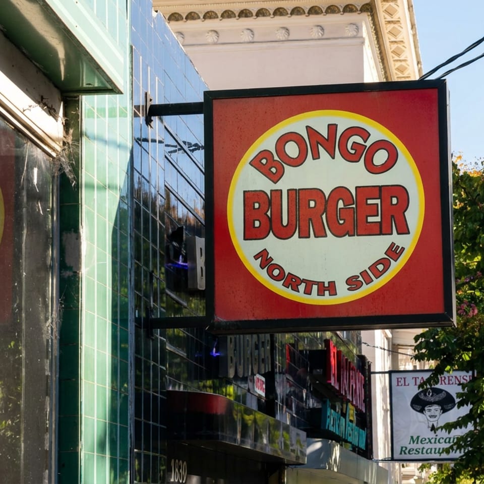 Street-facing Bongo Burger North Side sign outside a restaurant, with storefronts, trees, and neighboring businesses visible.