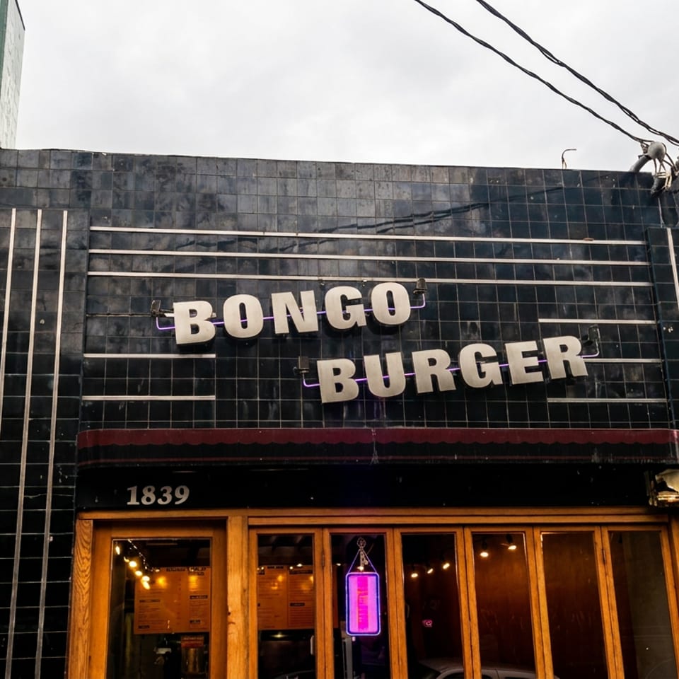 Street-facing Bongo Burger restaurant with black tiled facade, bold cream signage, and warmly lit wooden entrance.
