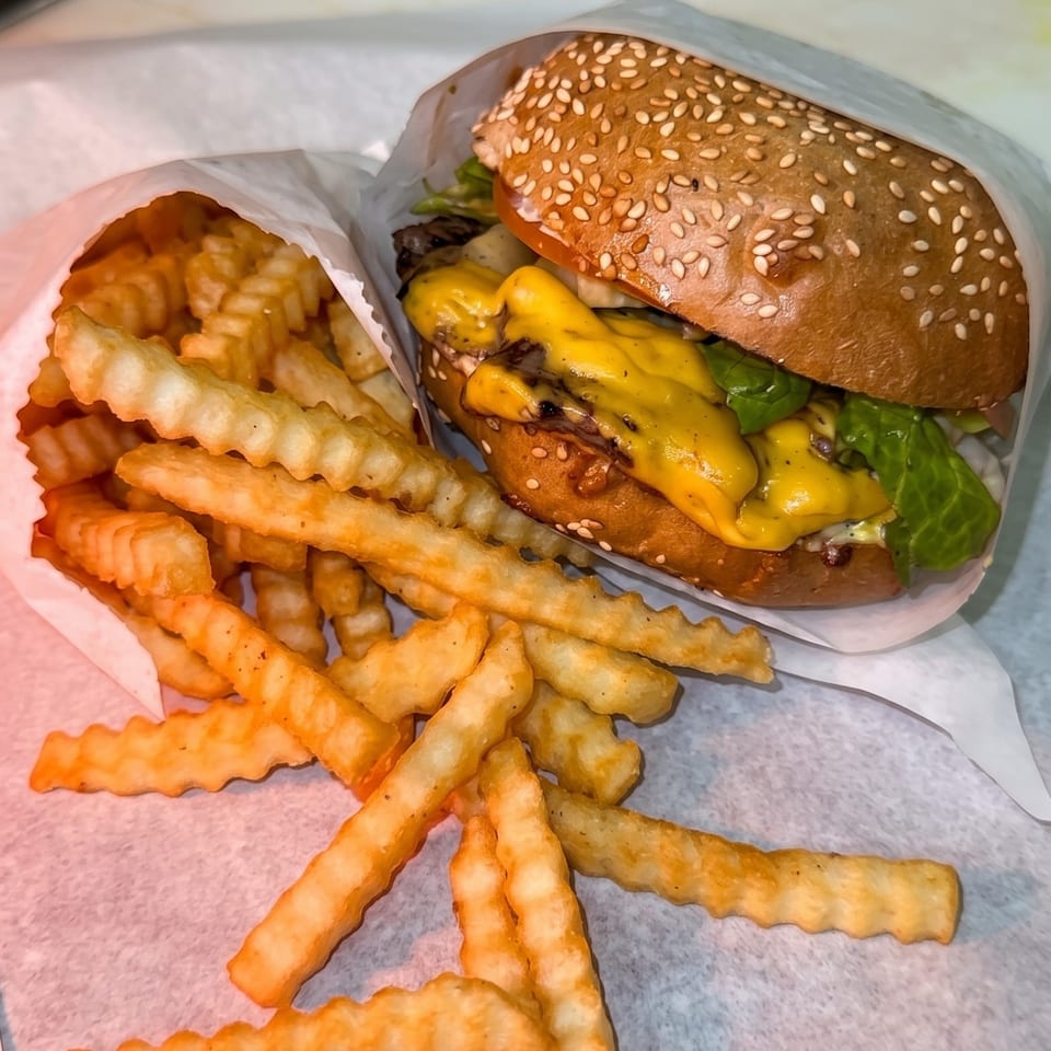Sesame-seed cheeseburger with lettuce beside a generous serving of crinkle-cut fries on a paper-lined tray.